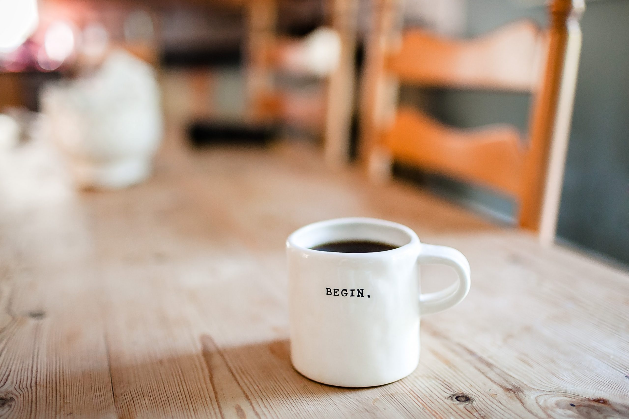 A white ceramic mug engraved with the word "begin" sits on a wooden table.
